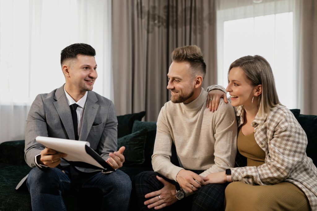 Real estate agent consulting a smiling couple on a couch in a cozy, indoor setting.