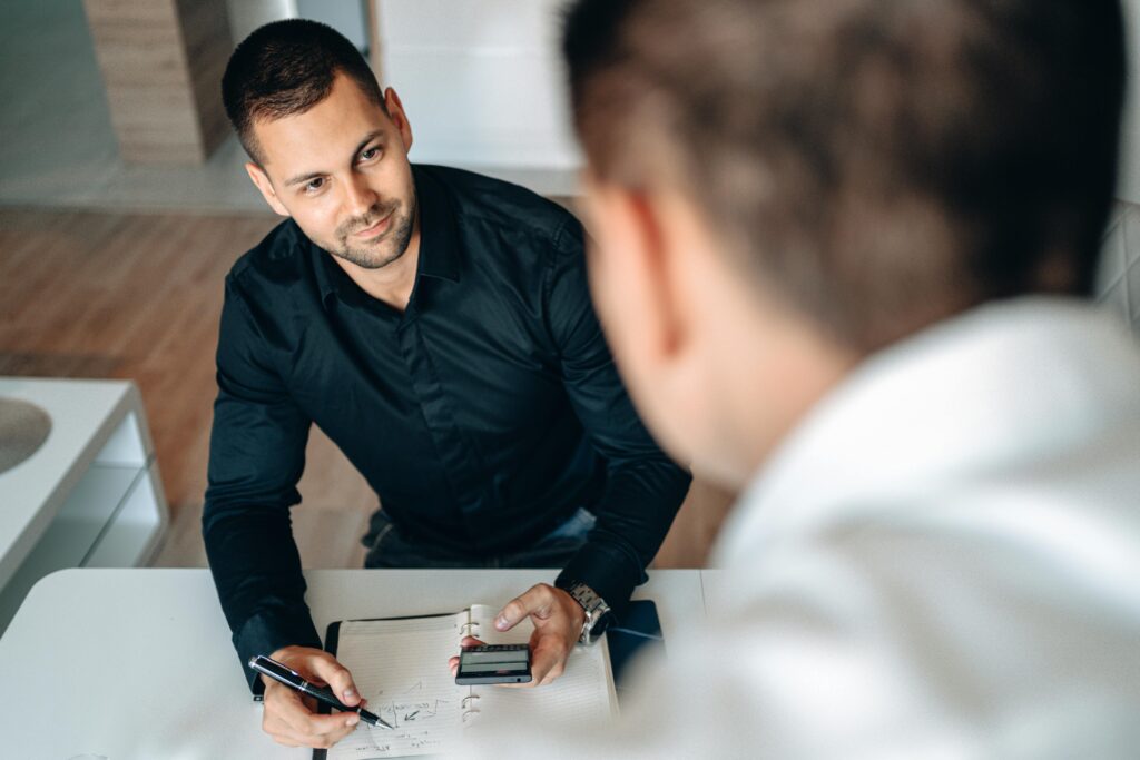 Two men in a business meeting indoors, discussing and taking notes.